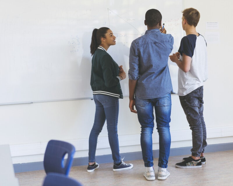Three young people in discussion in front of a whiteboard, one person is writing something