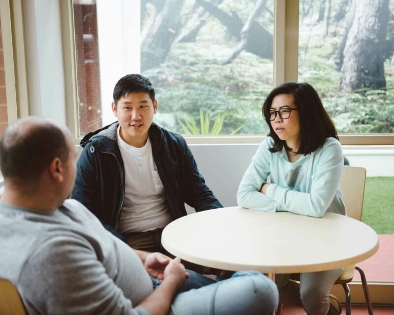 A group of three people sitting at a table at university in discussion.