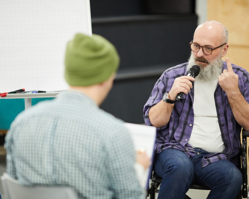 Older man with beard facilitating discussion. He uses a wheelchair.