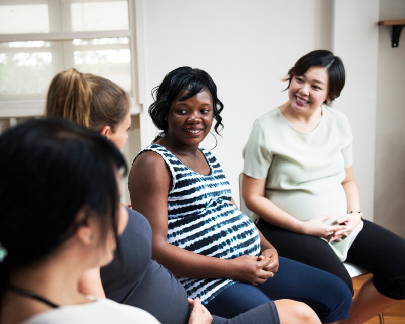 Pregnant women sitting in a group together, they are talking and being friendly with one another.